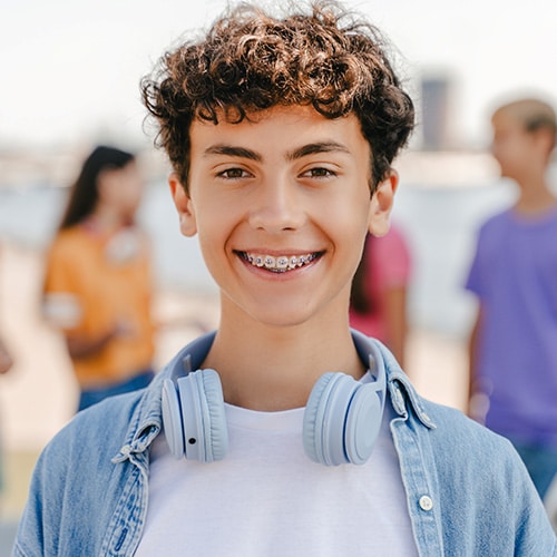 Teen smiling with braces and a pair of headphone around his neck